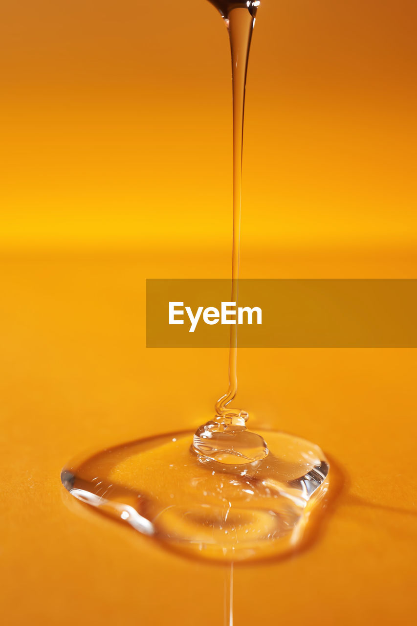 A drop of body gel or shampoo pouring from above on a yellow saturated background.