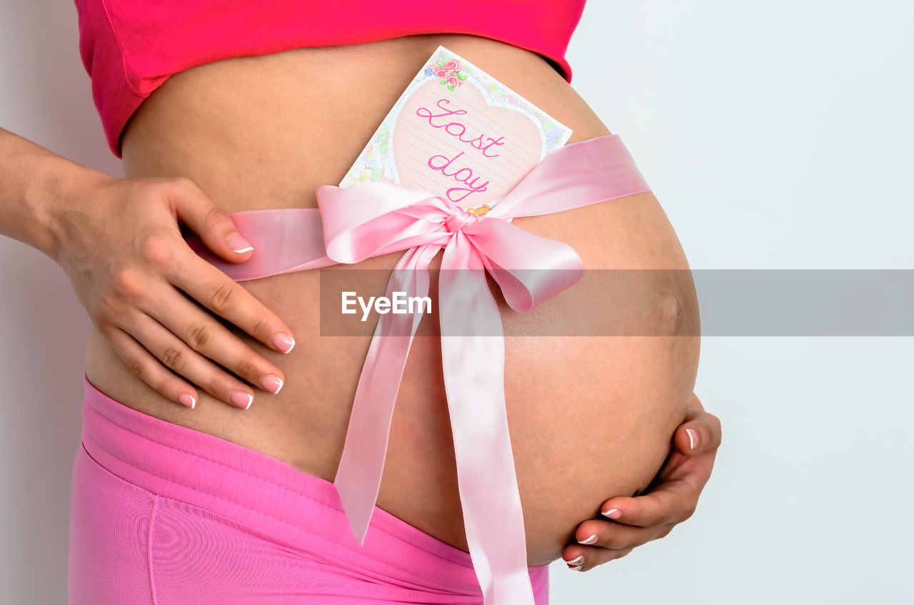 Midsection of pregnant woman with greeting card standing against white background