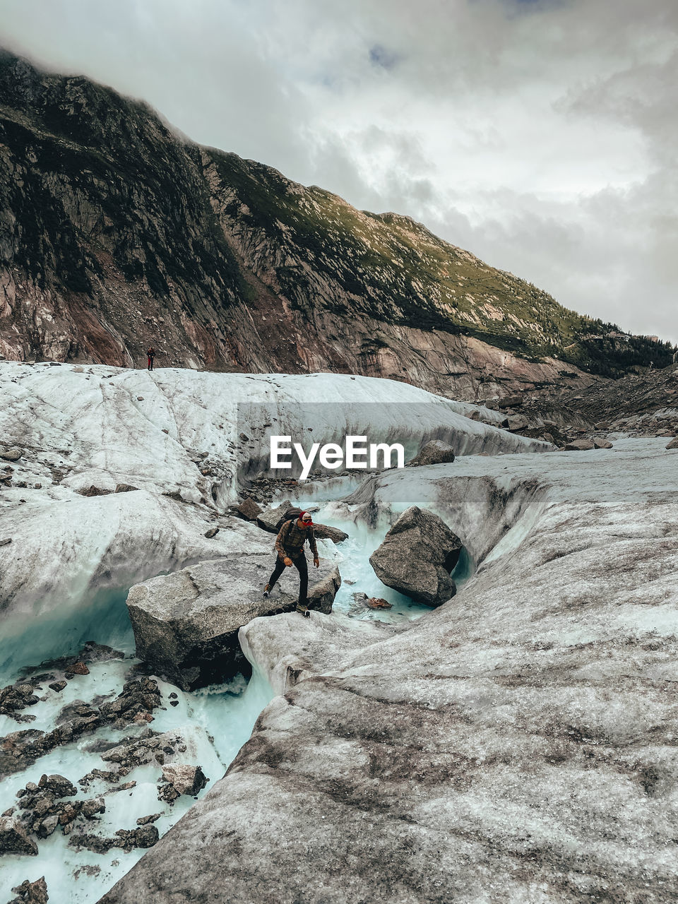 Climber stepping over rock in melt-water river on glacier mer de glace