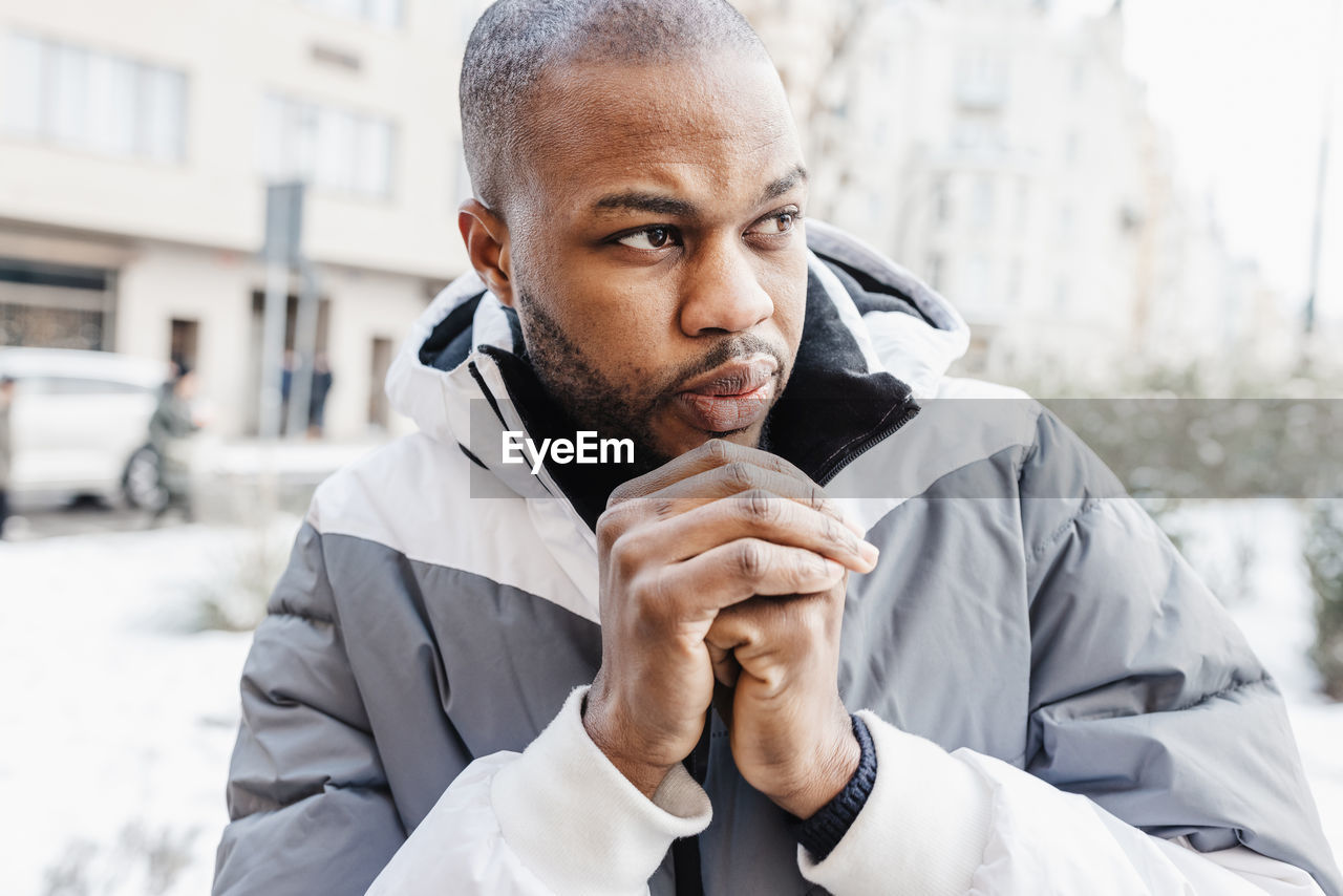 Young african man warming his cold hands with breath in winter