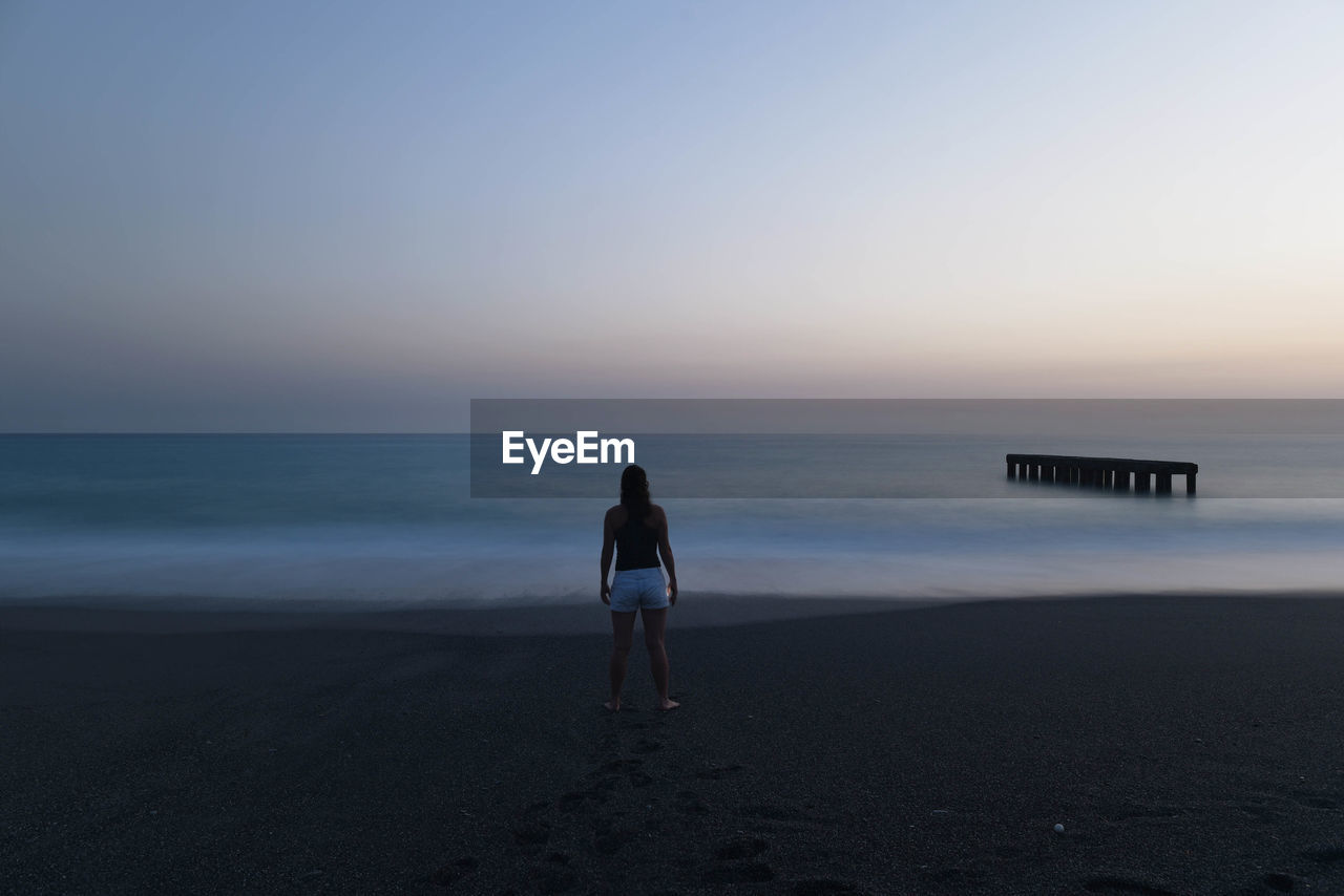 Rear view of woman standing on beach against clear sky