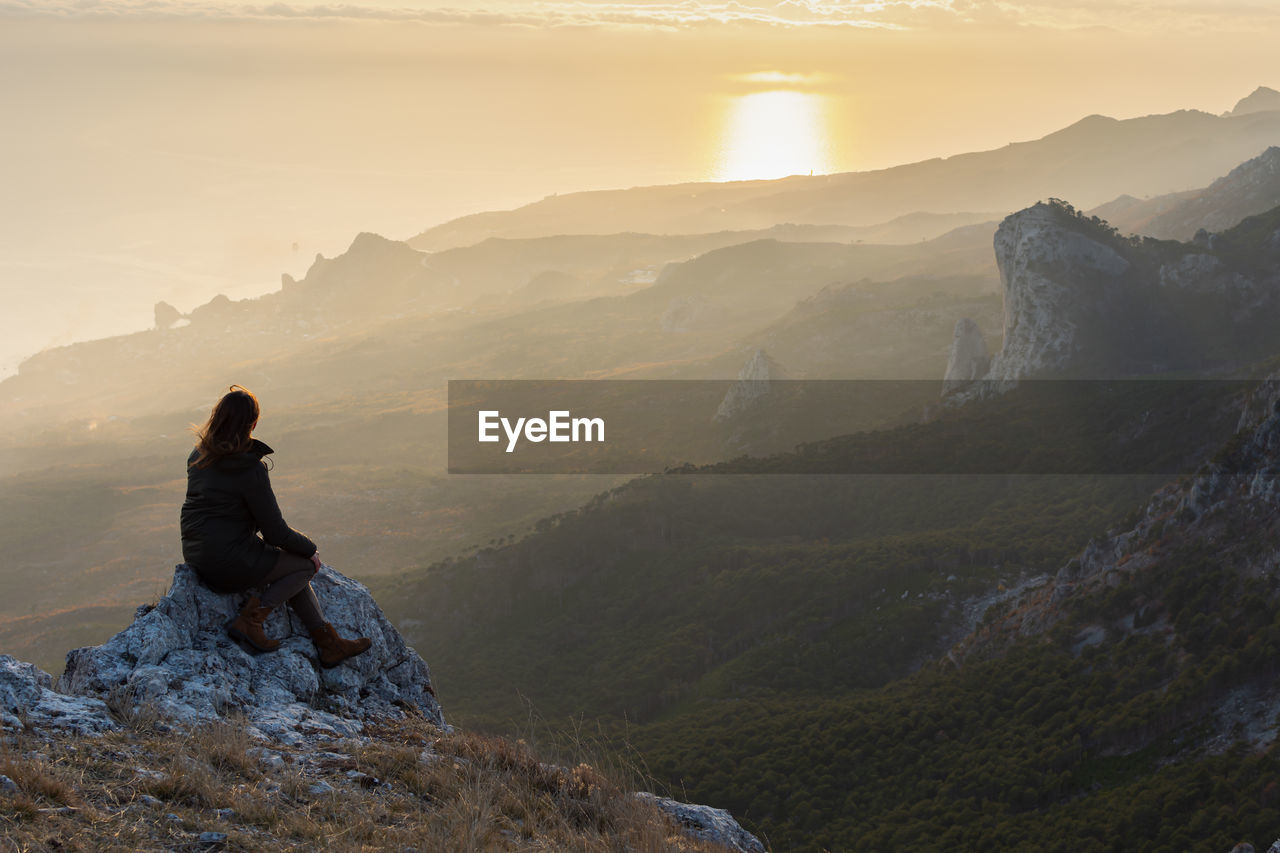 A girl stands on a mountain and looks at the sunset. atmospheric evening view of the mountains