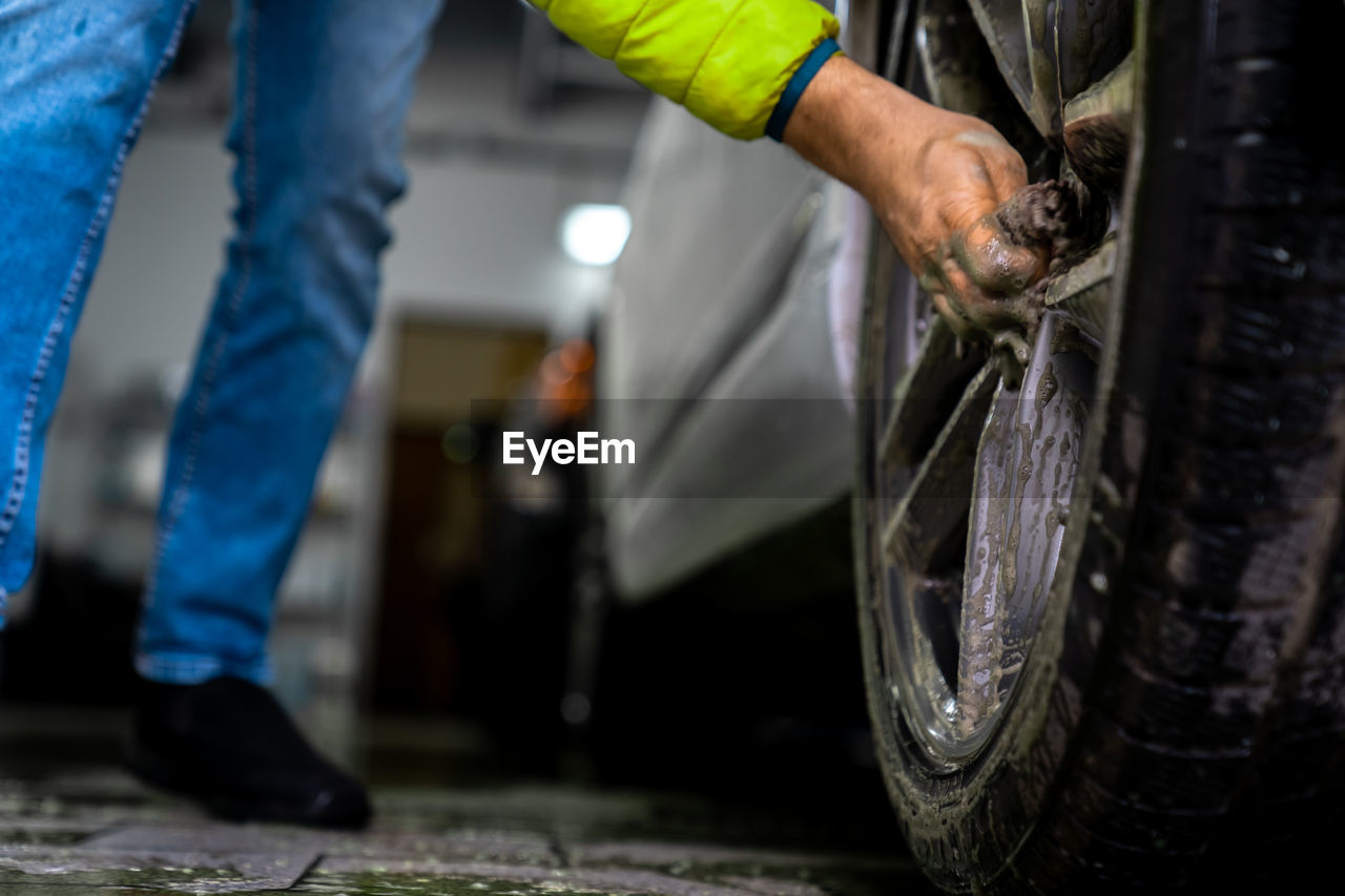 Low section of man cleaning tire at garage