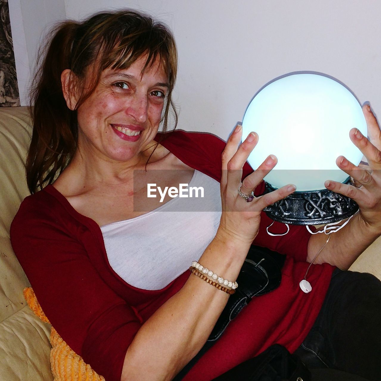 Portrait of smiling woman holding crystal ball while resting on sofa at home