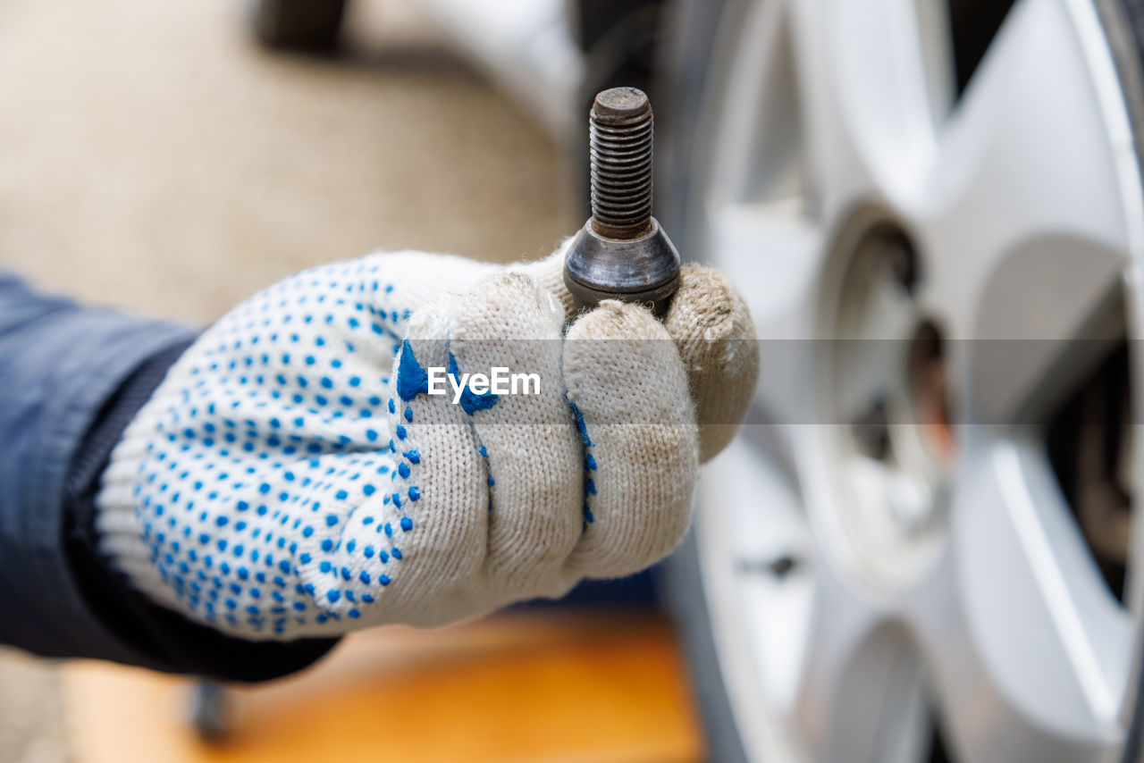 Mechanic hand in fabric glove holding car wheel bolt