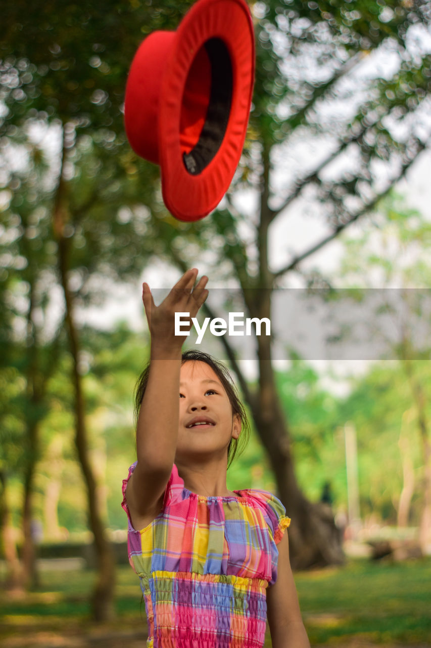 Cute little girl throwing a red hat in a summer green park.