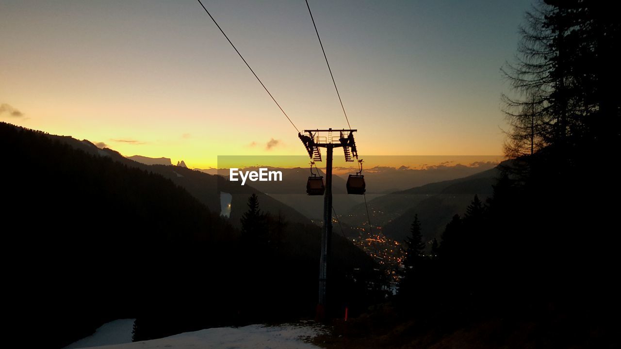 Low angle view of ski lift by mountains against sky during sunset