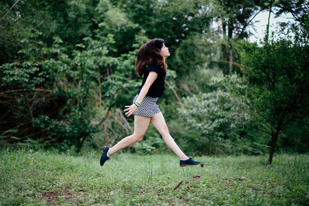 Full length of young woman jumping on grassy field