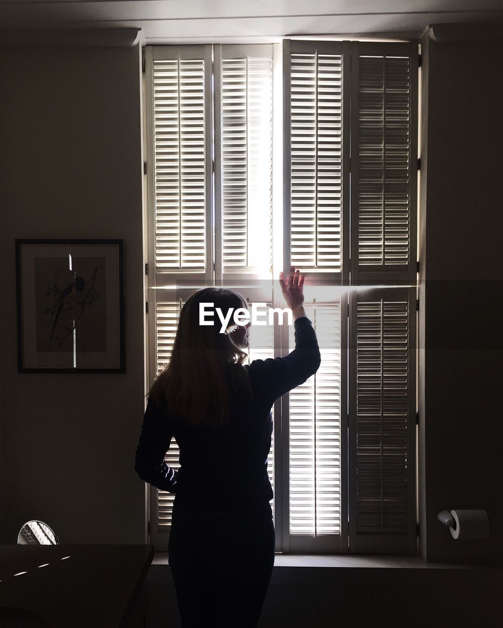 Rear view of woman holding window shutter at home