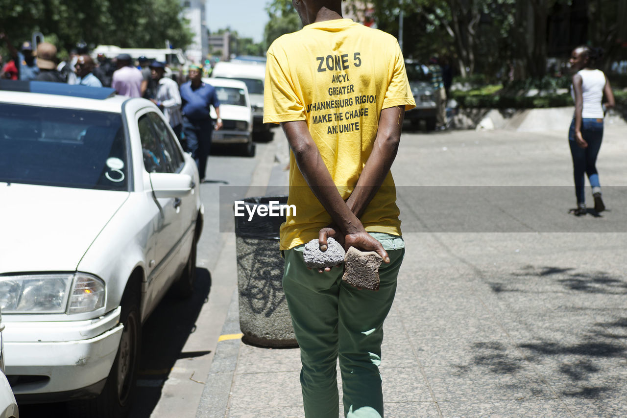 Rear view of man holding stones while walking on sidewalk