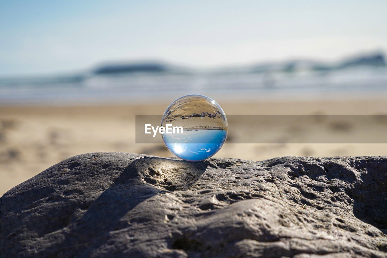 Photography crystal photo ball showing upside down reflection of sky beach and waves on rocks 