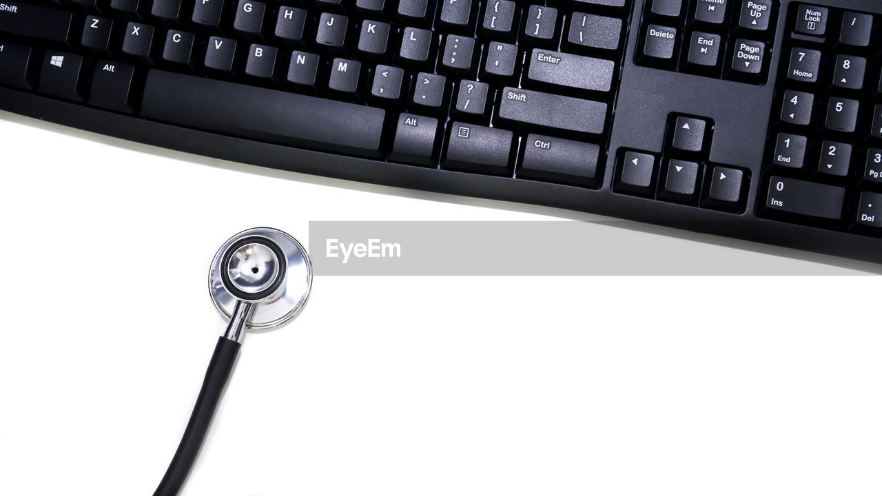 Close-up of stethoscope by computer keyboard over white background