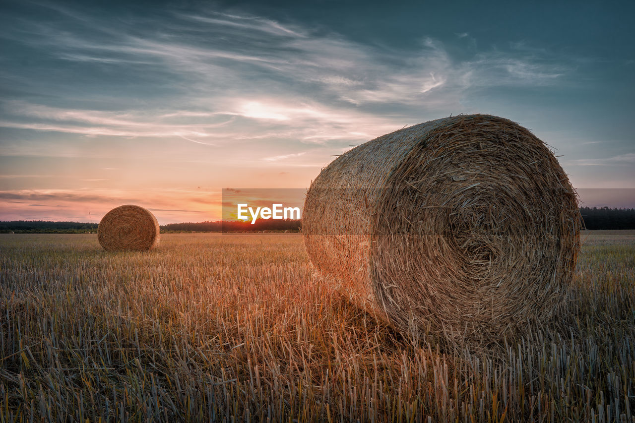 Hay bales on field against sky during sunset