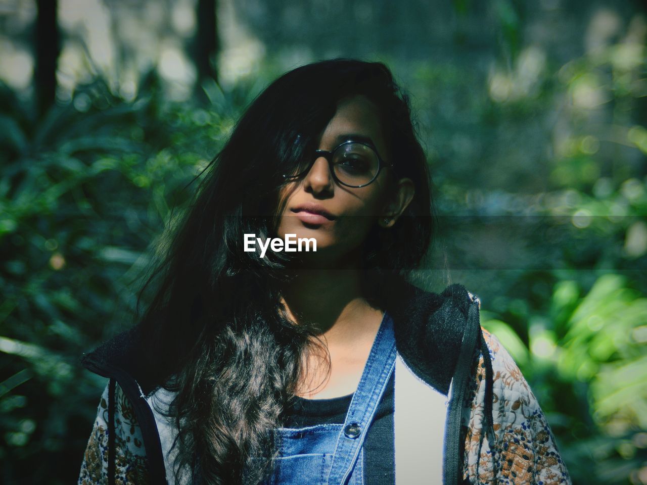 Portrait of young woman wearing eyeglasses while standing against plants