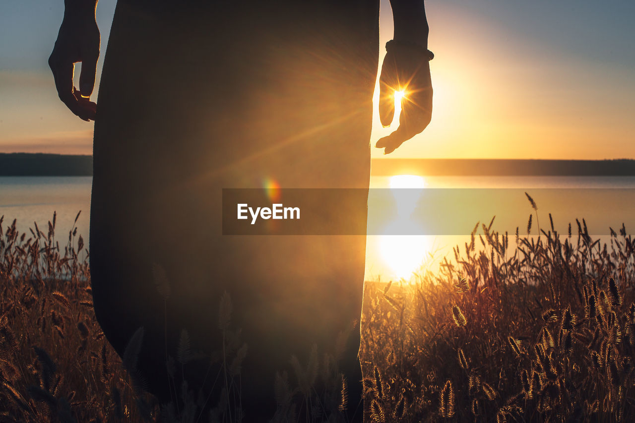 Midsection of man standing by sea against sky during sunset