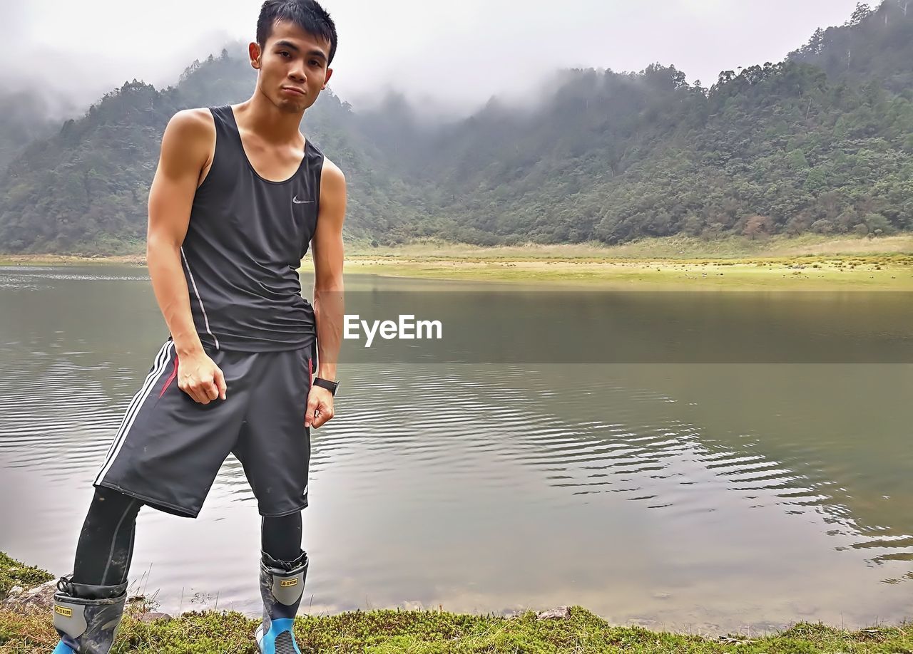 YOUNG MAN STANDING AGAINST LAKE