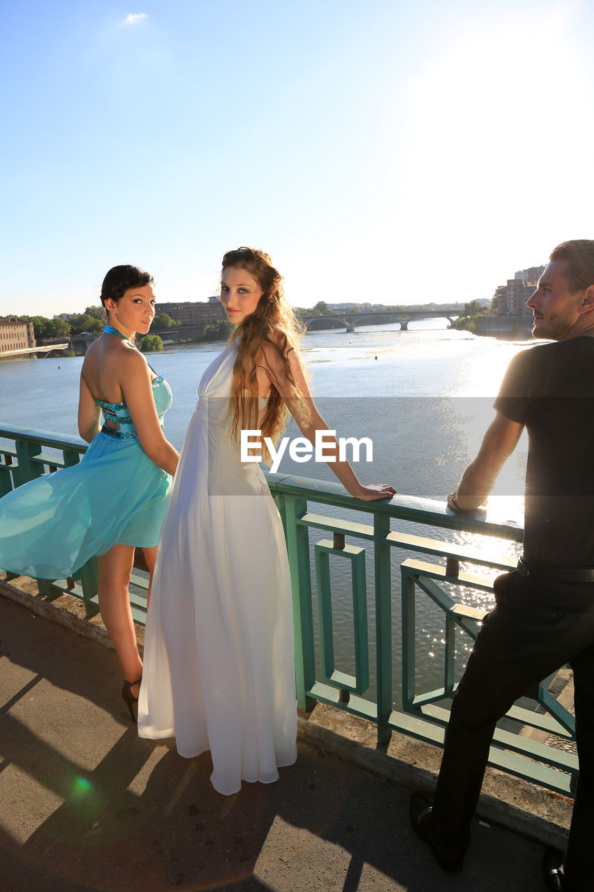 Portrait of beautiful women standing by railing on sunny day