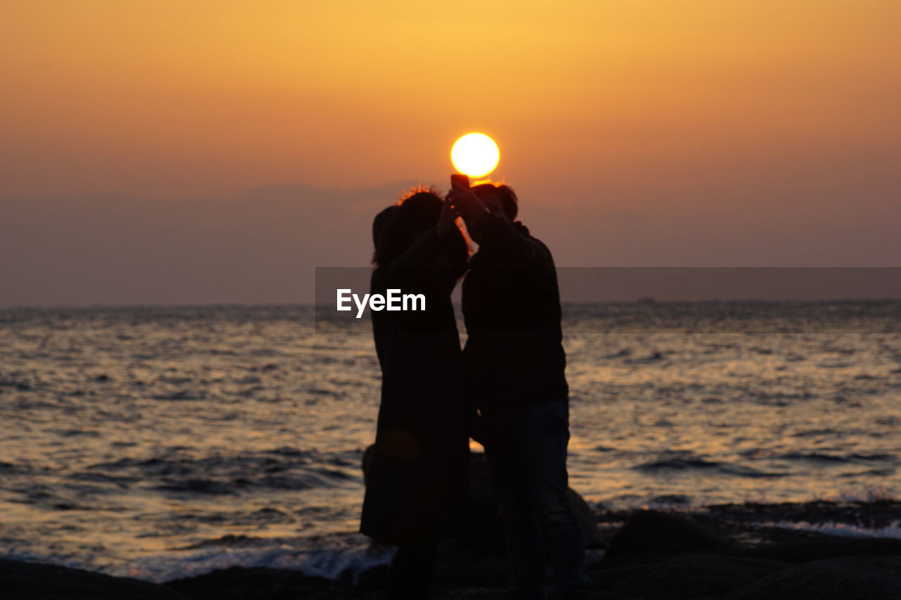 Silhouette man and woman standing at beach during sunset