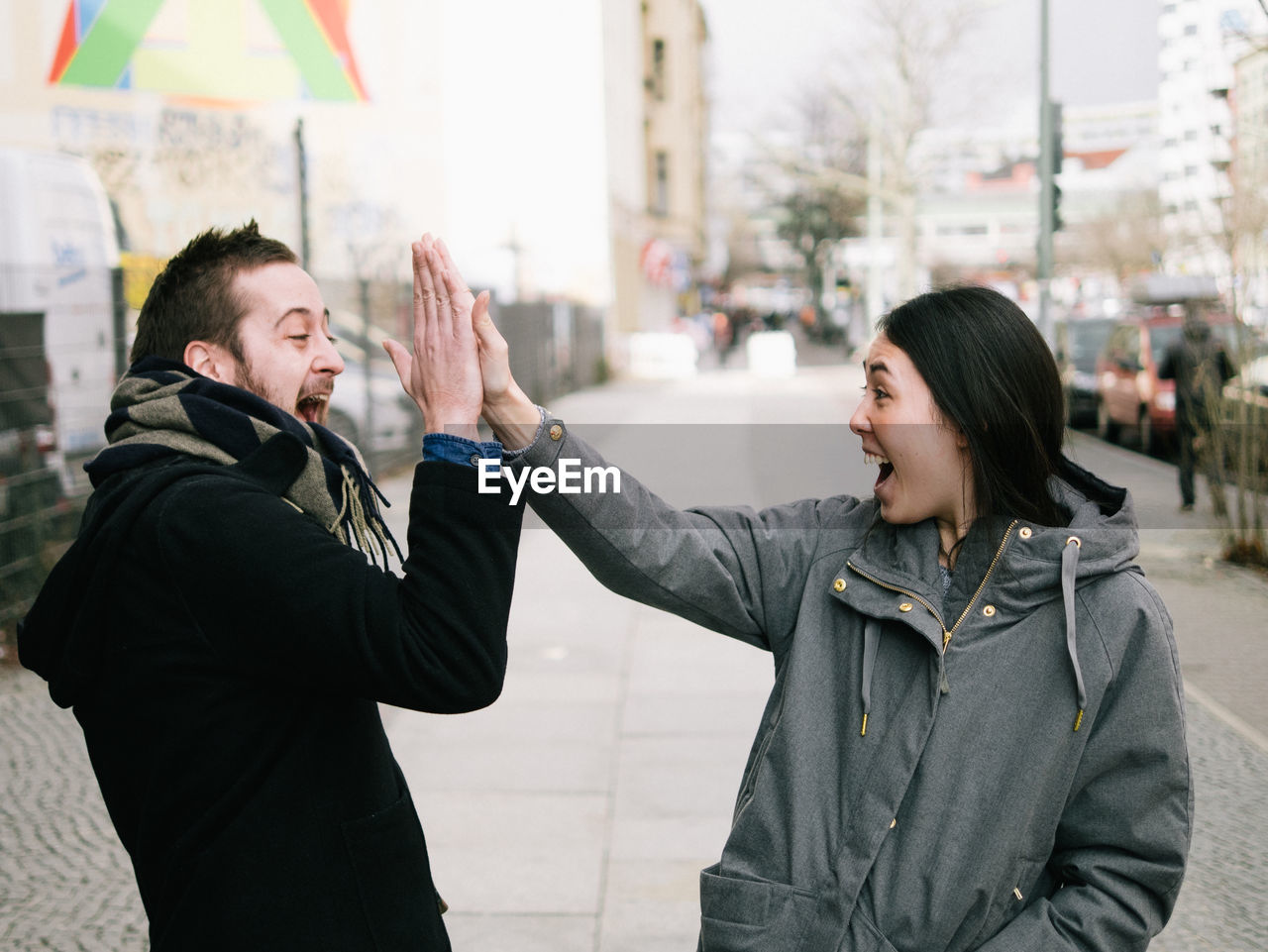 Excited friends giving high-five on sidewalk in city
