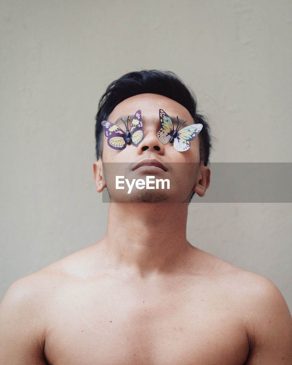 Shirtless man with artificial butterflies against gray wall