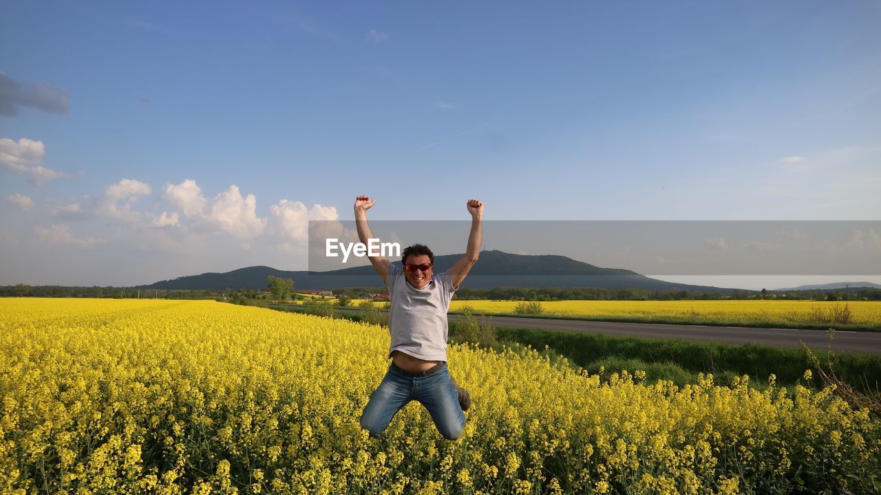 Portrait of happy man jumping on land against sky