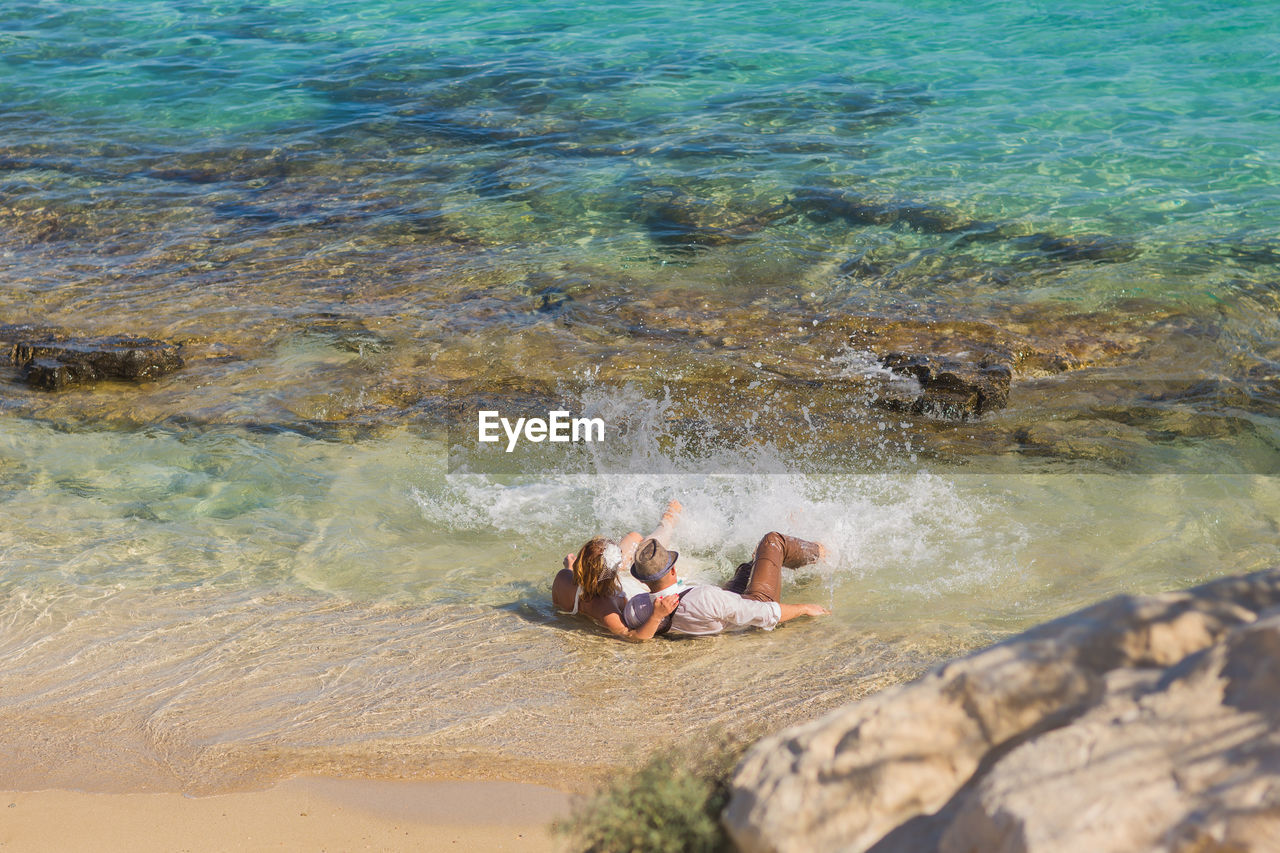 HIGH ANGLE VIEW OF WOMAN RELAXING ON ROCK AT SEA