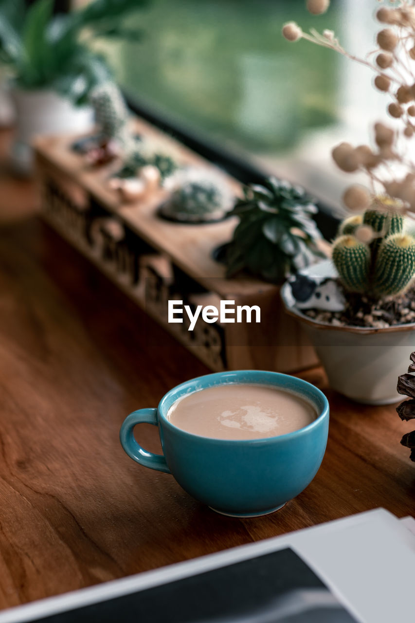Close-up of coffee cup with potted plant on wooden table