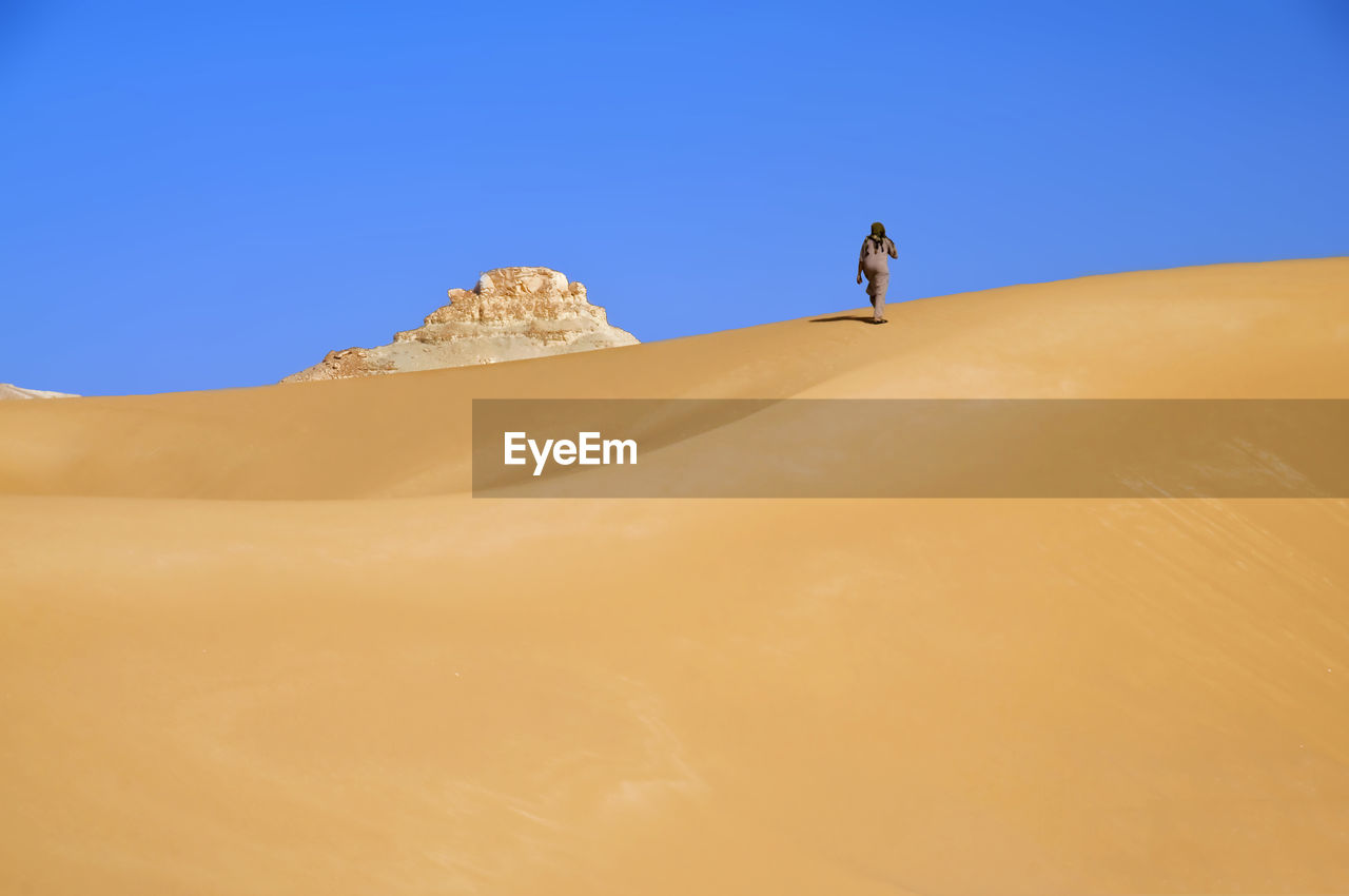 Low angle view of man climbing sandy hill at desert against clear sky