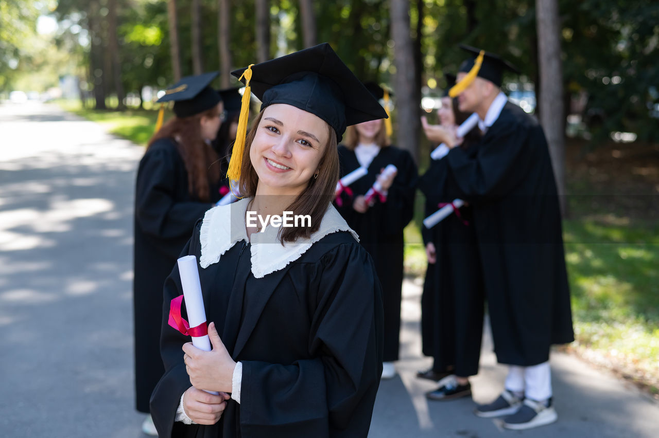 portrait of young woman wearing graduation gown standing in forest