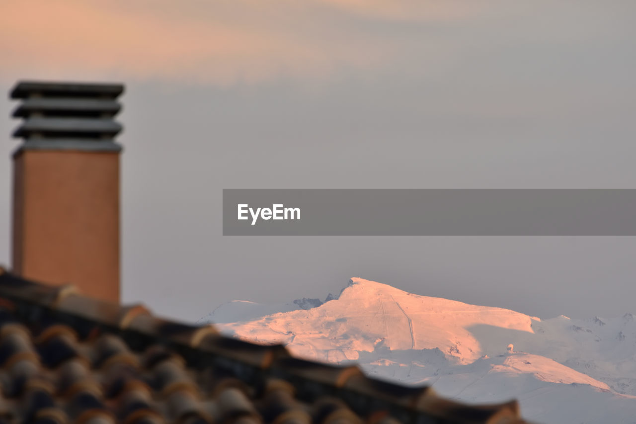 SCENIC VIEW OF BUILDING BY MOUNTAINS AGAINST SKY DURING SUNSET