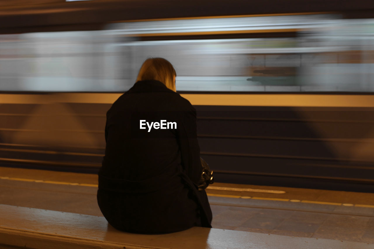 Rear view of woman sitting in front of train at railroad station platform