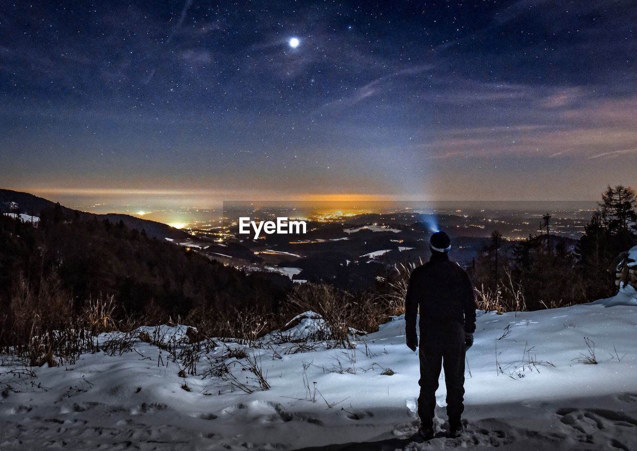 Rear view of man standing on snowcapped mountain against star field