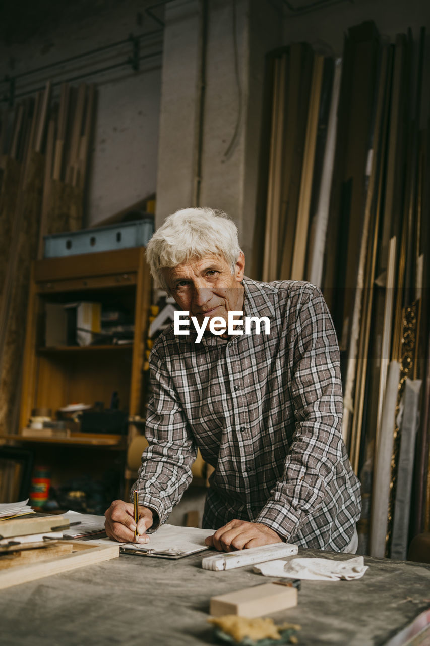 Portrait of senior male entrepreneur leaning on workbench at workshop