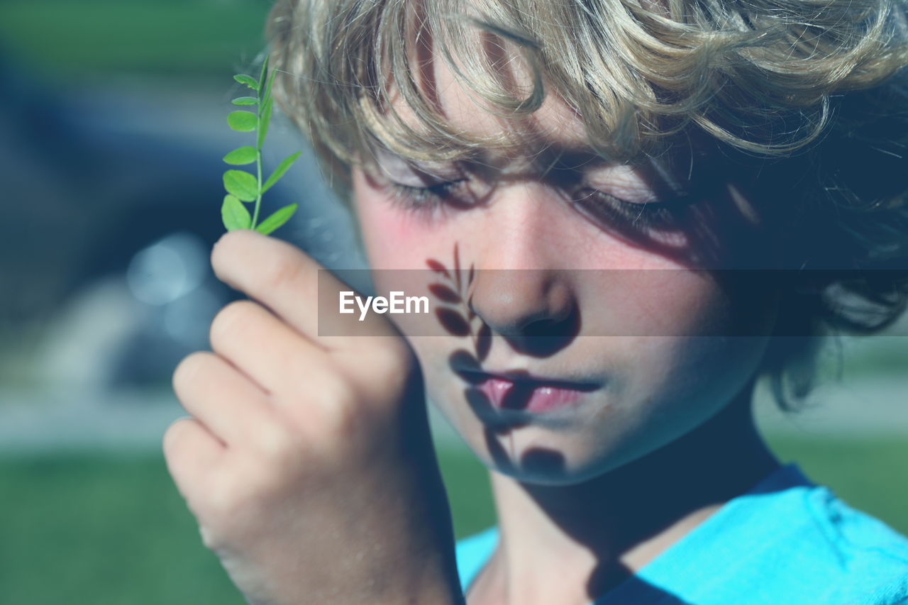 Close-up of blond boy holding leaves with closed eyes on sunny day