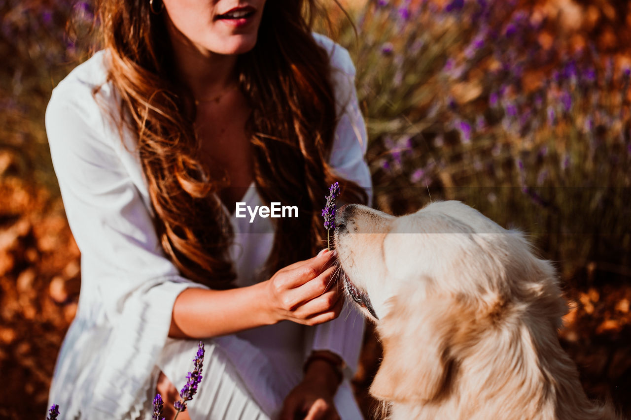 Midsection of woman with dog by flowering plants against sky