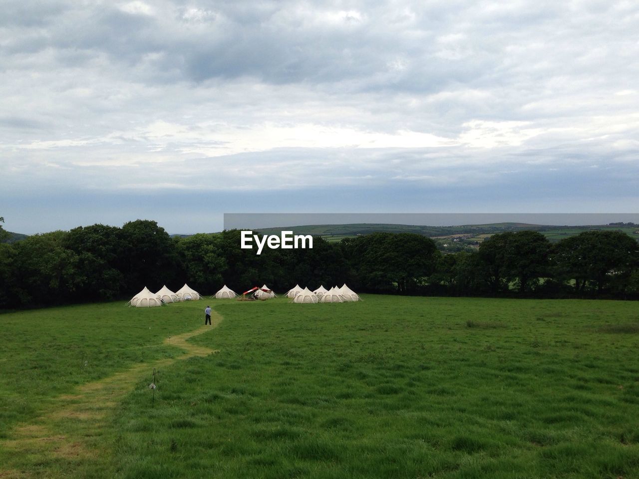 Tents on green landscape against cloudy sky