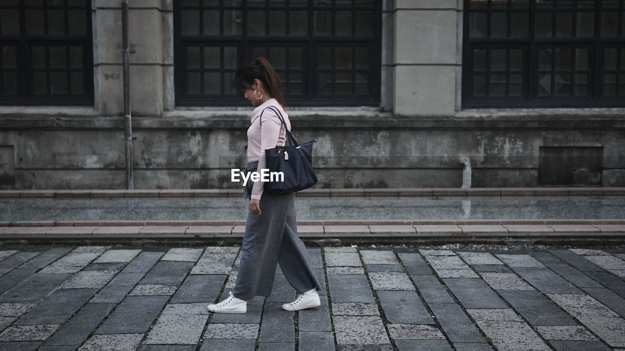 Side view of mid adult woman with purse walking on footpath against building in city