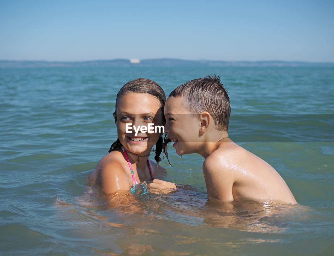 Siblings swimming in sea against clear sky