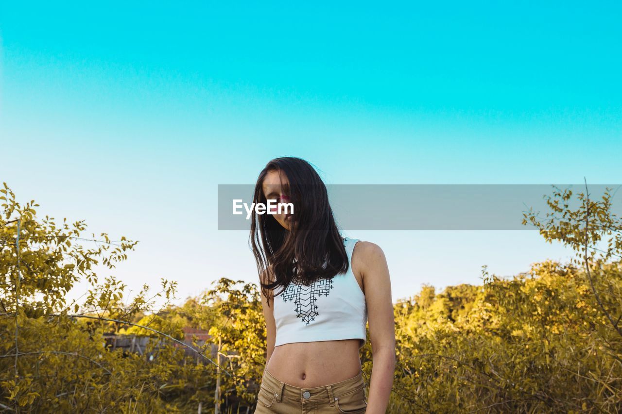 Woman standing by plants against clear sky