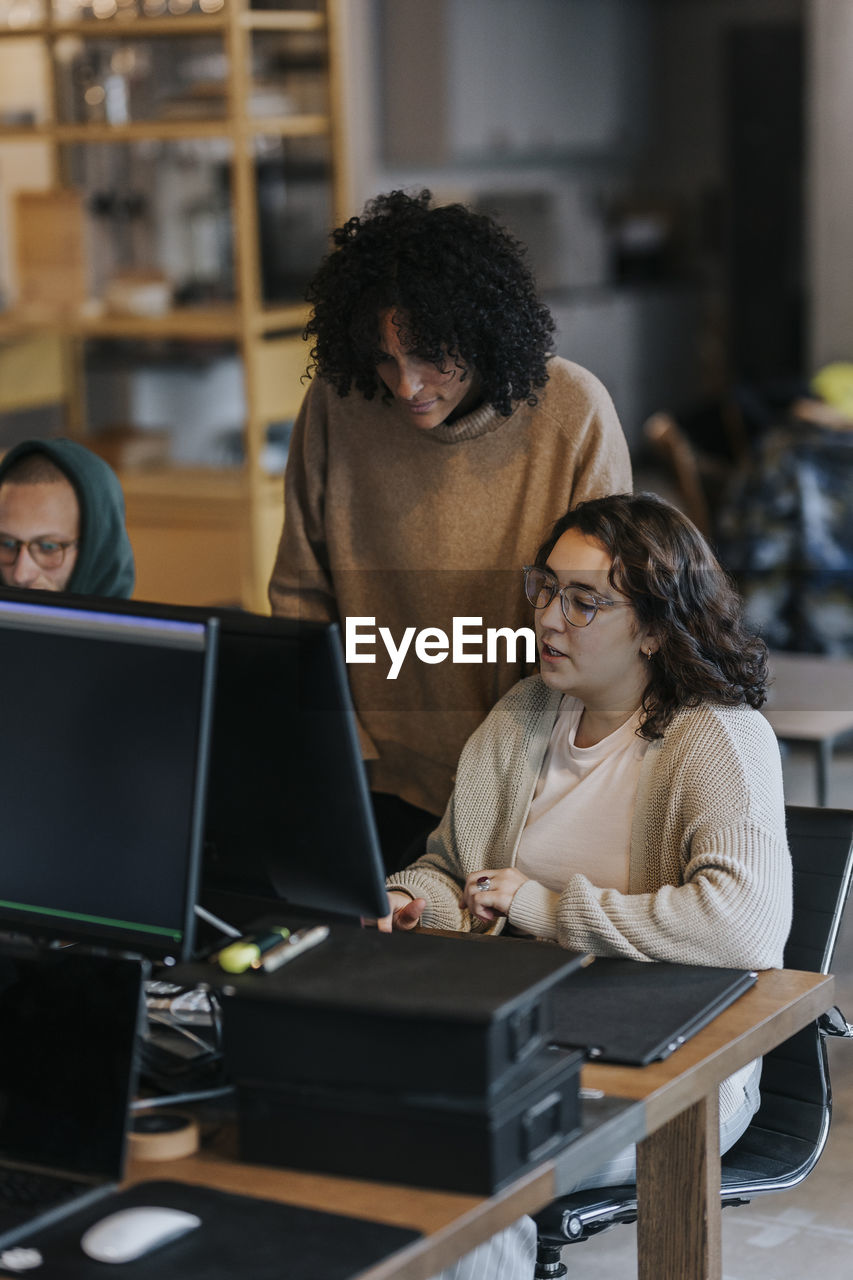 Multiracial business colleagues discussing over computer at desk in office