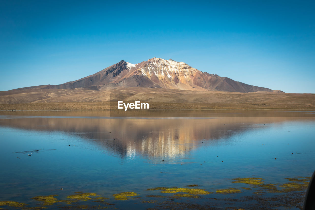 Scenic view of lake and mountains against clear blue sky
