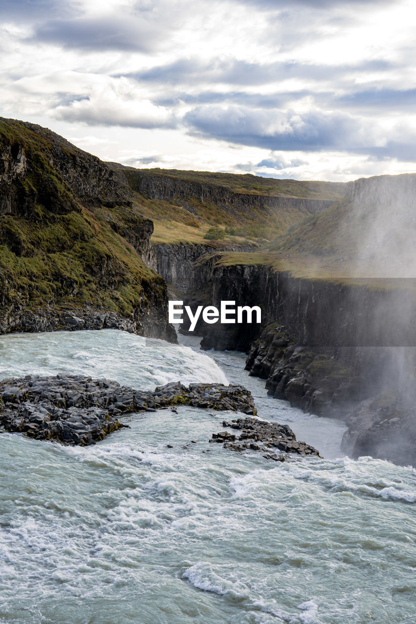 scenic view of waterfall against cloudy sky