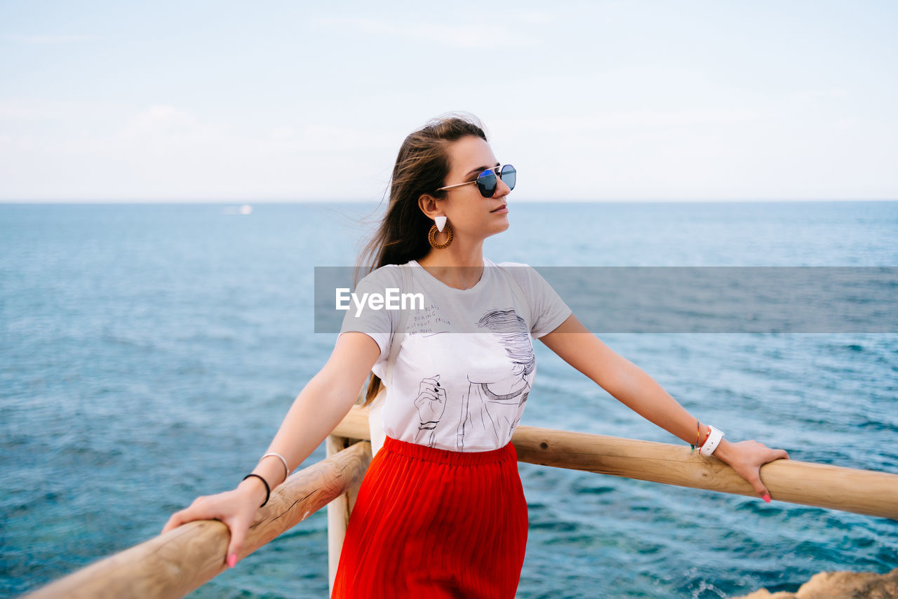 YOUNG WOMAN LOOKING AT SEA AGAINST SKY