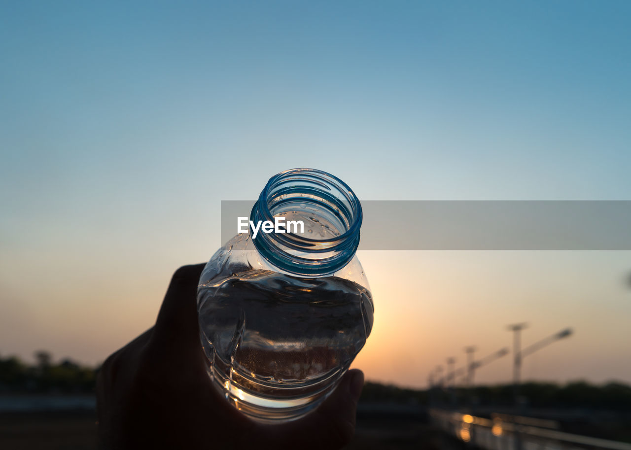 Cropped image of person holding bottle during sunset