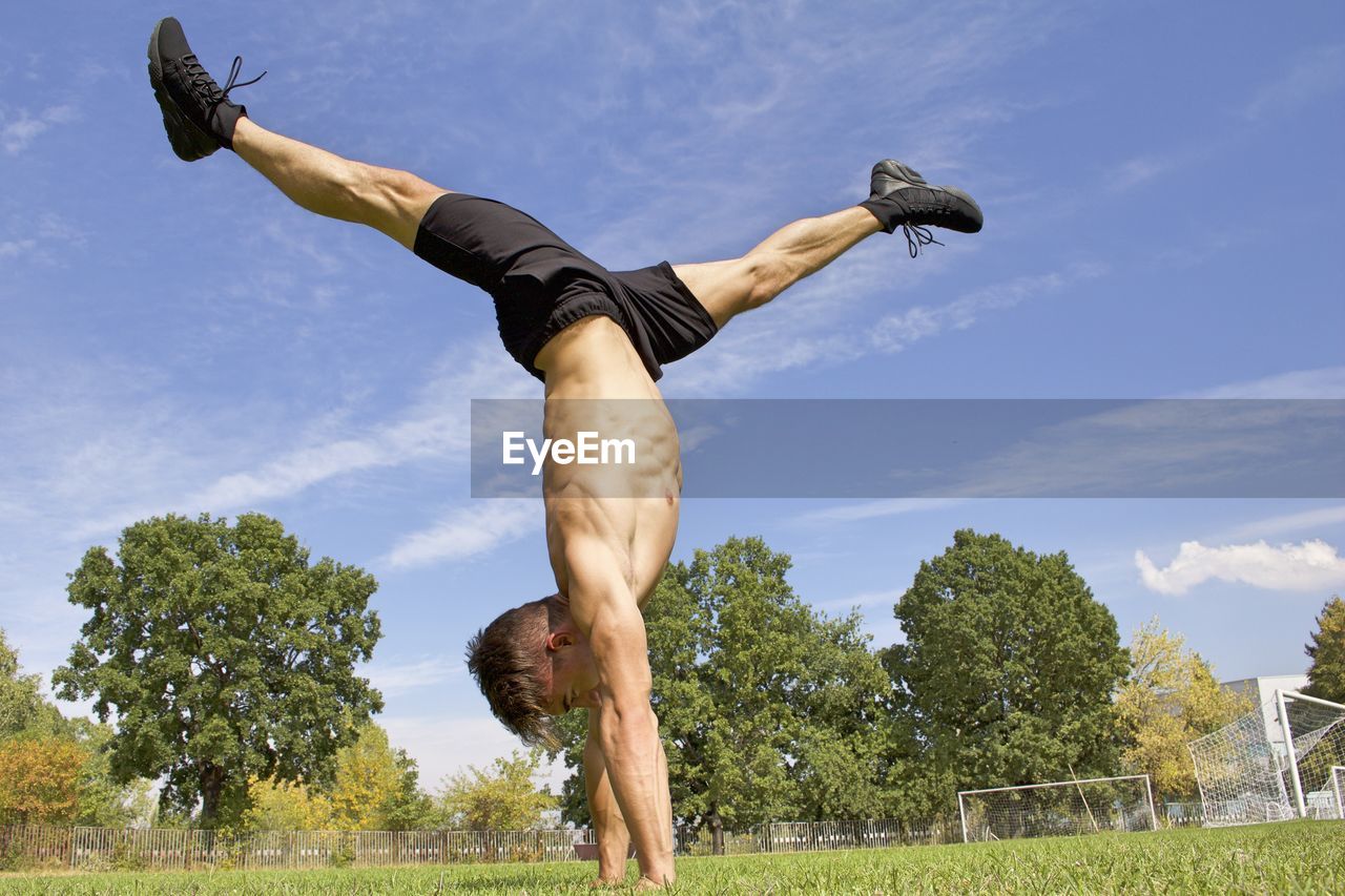 Shirtless man doing handstand on field against sky