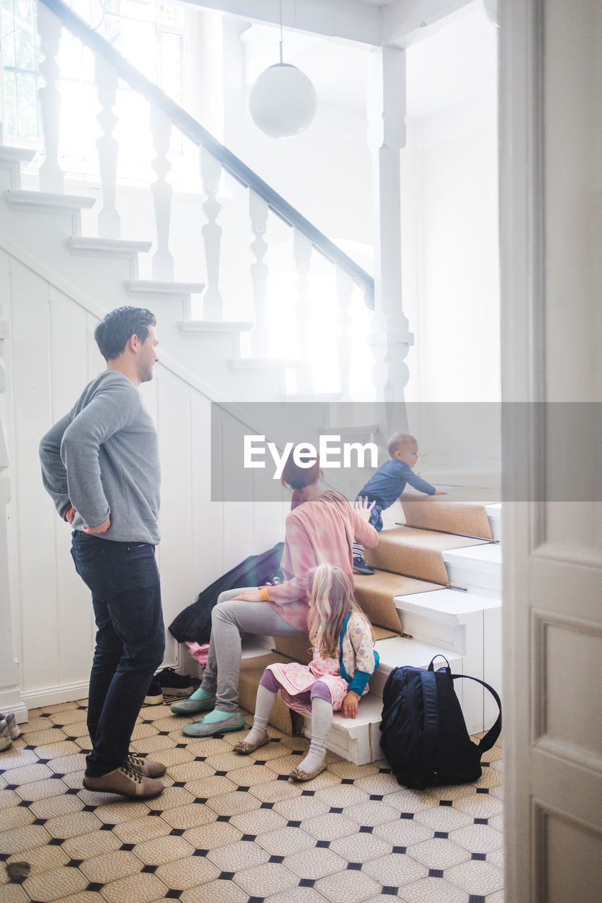 Full length of father looking at family sitting on steps