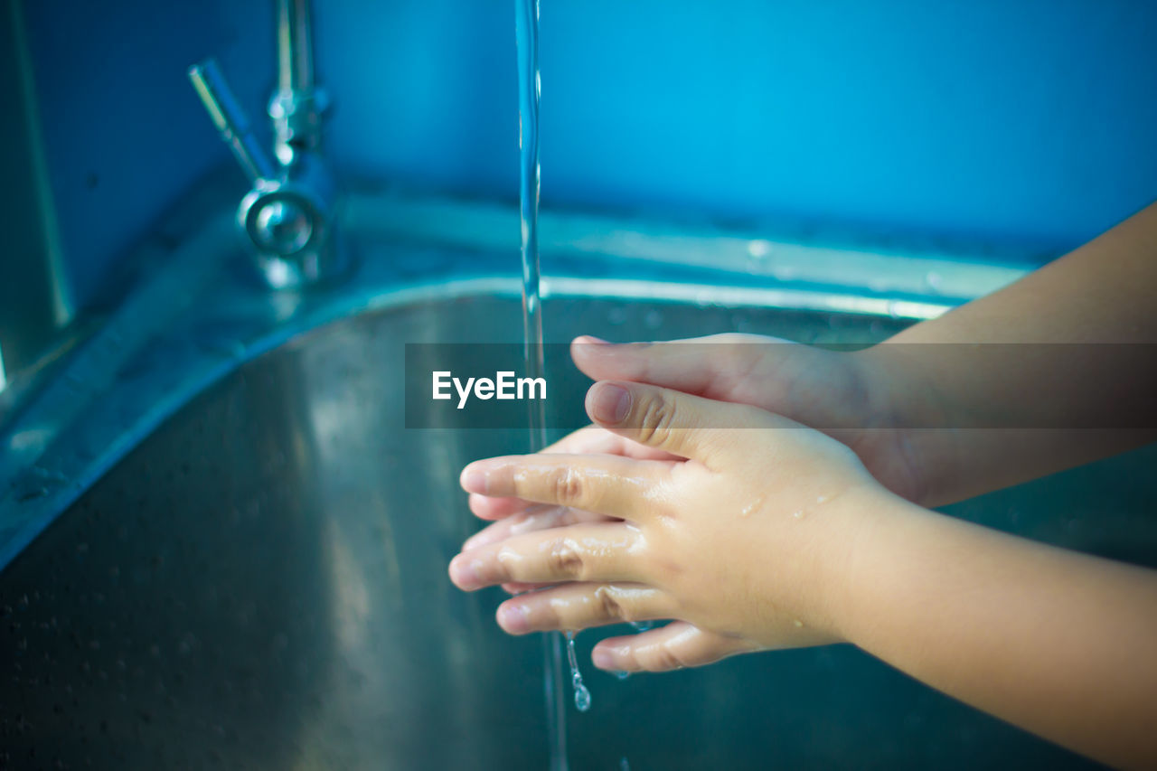 Close-up of child washing hand under faucet