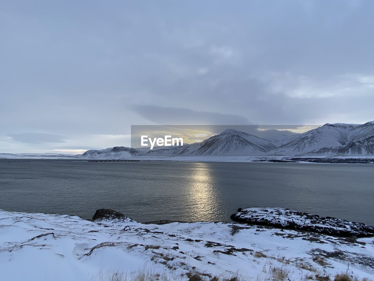 Scenic view of frozen lake by snowcapped mountains against sky