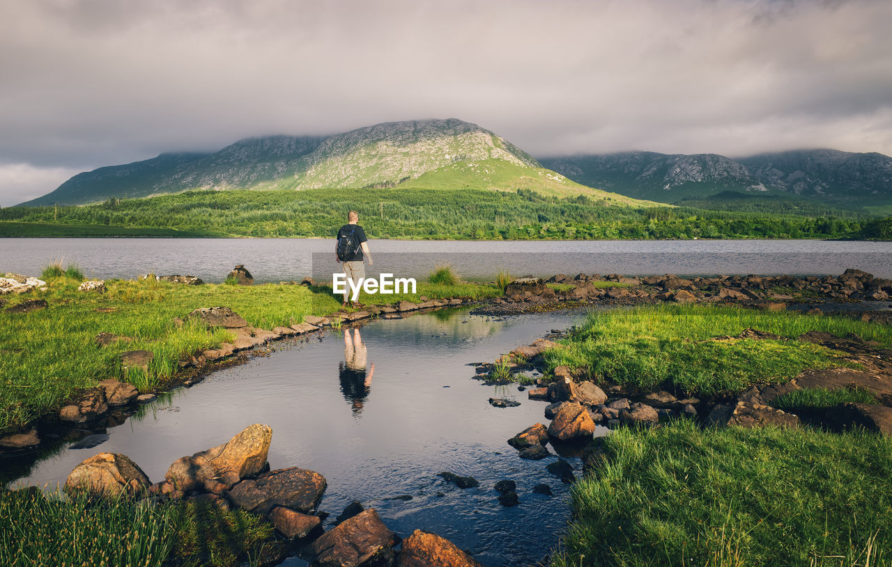 Travel and lifestyle concept, backpacker hiker reflected in lough inagh, mountains, galway, ireland 