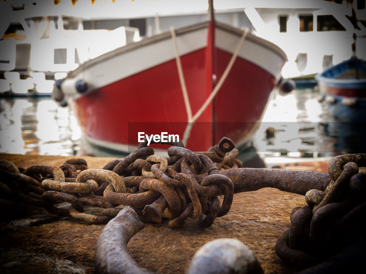 Close-up of rusty metallic chain against red boat at harbor